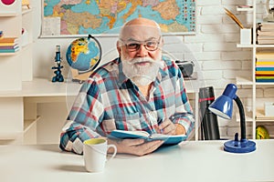 Portrait of senior teacher sitting at desk in classroom. Teaching in university. University education.