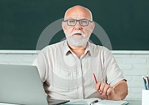 Portrait of senior teacher teaching line of high school students with computer laptop in classroom on blackboard. Adult