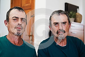 Portrait of senior twin men smiling on camera indoors at home - Focus on faces