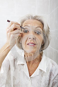 Portrait of senior woman applying eyeliner in bathroom