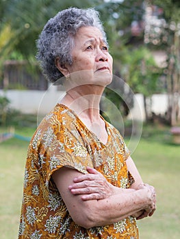 Portrait of a senior woman with arms raised and looking up while standing in a garden. Concept of aged people and healthcare