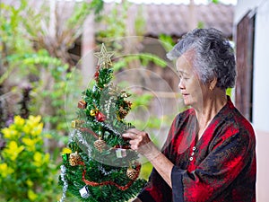 Portrait of senior woman decorating the Christmas tree with colorful ribbons at home. Concept of aged people and festival