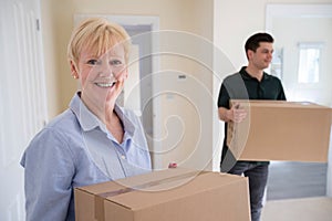 Portrait Of Senior Woman Downsizing In Retirement Carrying Boxes Into New Home On Moving Day With Removal Man Helping