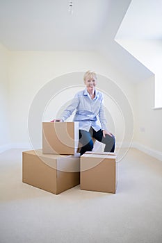 Portrait Of Senior Woman Downsizing In Retirement Sitting On Boxes In New Home On Moving Day photo