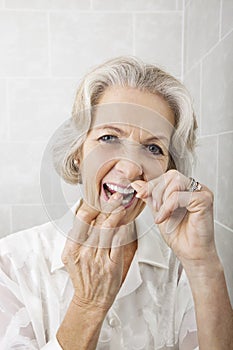 Portrait of senior woman flossing teeth in bathroom