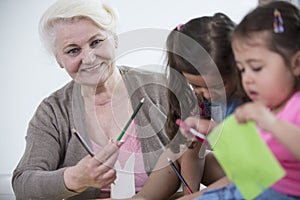 Portrait of senior woman helping granddaughters in making handicrafts at home