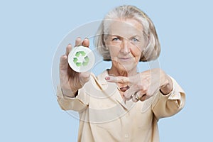 Portrait of senior woman holding badge with recycling symbol against blue background