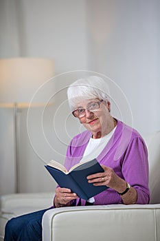 Portrait of a senior woman at home using a book