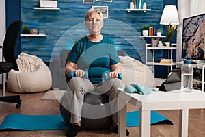 Portrait of senior woman looking into camera while sitting on swiss ball training body muscles