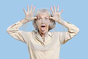 Portrait of senior woman making funny faces with hands on head against blue background