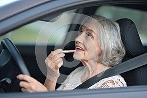 Portrait of senior woman putting lipstick in the car