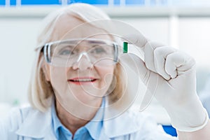 Portrait of senior woman scientist analyzing pill in hand