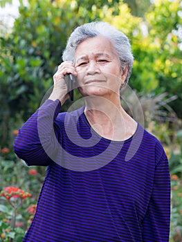 Portrait of a senior woman with short gray hair using a smartphone while standing in a garden. Concept of aged people
