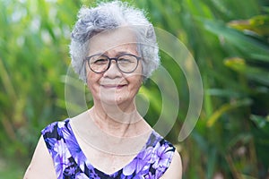 Portrait of a senior woman with short gray hair, wearing glasses, smiling and looking at the camera while standing in a garden.