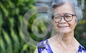Portrait of a senior woman with short gray hair, wearing glasses, smiling, and looking at the camera while standing in a garden.