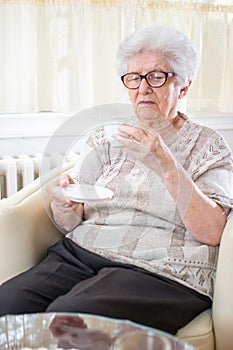 Portrait of senior woman sitting on armchair and drinking coffee at home