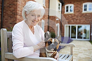 Portrait Of Senior Woman Sitting On Bench With Pet French Bulldog In Assisted Living Facility photo