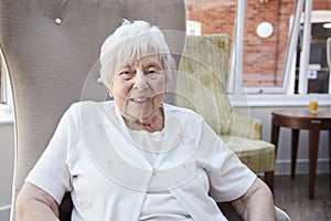 Portrait Of Senior Woman Sitting In Chair In Lounge Of Retirement Home