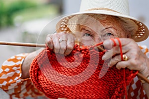 Portrait of senior woman sitting outdoor and knitting red scarf.