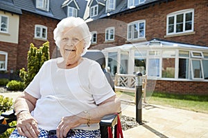 Portrait Of Senior Woman Sitting Outside Retirement Home In Motorized Wheelchair photo
