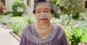 Portrait of senior woman smile, relax in assisted living retirement facility, happy and carefree in a garden. Safety