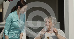 Portrait of Senior Woman Taking Pills Nurse is Giving Medicine Smiling Together at Nursing Home Outdoors on Sunny Day Shot on Red