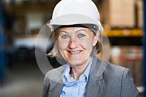 Senior woman warehouse manager or supervisor with white helmet.