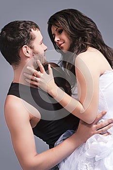 Portrait of Sensual Flirting Caucasian Couple Posing Together. Woman Embracing Man And Touching Cheek Against Gray