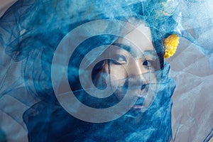 Portrait of sensual gorgeous asian woman looking at camera through blue veil on face