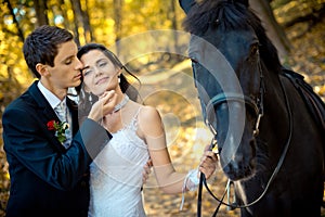 Portrait of the sensual newlyweds and horse. The handsome groom is gently stroking the face of his adorable bride