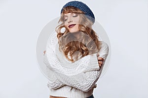 Positive blond woman in sweater and hat on white background