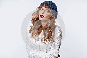 Positive blond woman in sweater and hat on white background