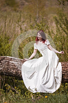 Portrait of Sensual Redhaired Girl in White Dress Outdoors. Posing on Wood Pile Against Sun