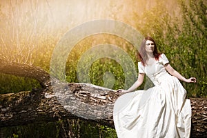 Portrait of Sensual Redhaired Girl in White Dress Outdoors. Posing on Wood Pile Against Sunlight