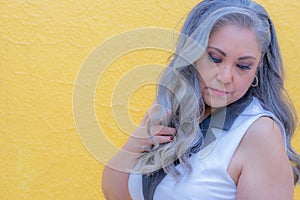 Portrait of sensual senior adult woman standing with her head turned down against yellow background