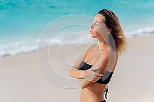 Portrait of sensual tanned girl in black swimsuit on sandy beach