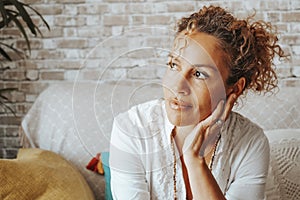 Portrait of serene woman looking outside the window at home having relax time sitting on the couch. Happy and confident female