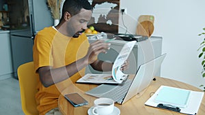 Portrait of serious African American businessman working with documents looking at laptop screen at home