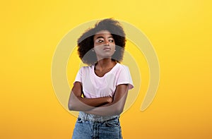 Portrait of serious african american lady looking aside and posing with folded arms over yellow studio background