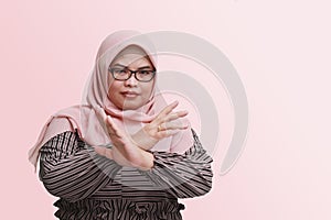 Portrait of serious Asian woman with hijab, showing X sign of hands for refusing an invitation from someone. Isolated image on