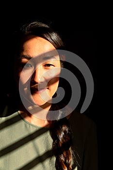 Portrait of serious asian woman standing in ray of light at home