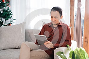 Portrait of serious asian young man sitting on a couch holding a