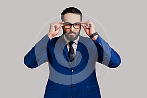 Bearded businessman putting off eyeglasses and looking at camera with bossy expression.