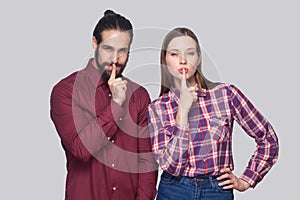 Portrait of serious bearded man and woman in casual style standing and looking at camera with fingers on lips and showing silent