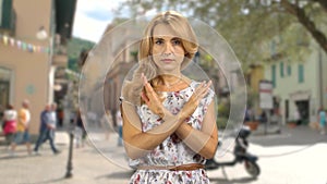 Portrait of a serious blond woman standing outdoors cross her arms as a sign of prohibition.