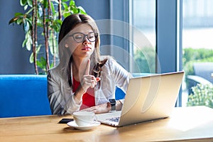 Portrait of serious bossy beautiful stylish brunette young woman in glasses sitting, looking at her laptop screen on video call