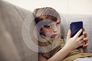 Portrait Of Serious Boy Sitting On Sofa At Home Gaming On Hand Held Devices At Home photo