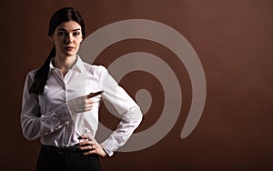 Portrait of serious brunette business woman pointing her finger to the side in studio on brown background with copyspace.