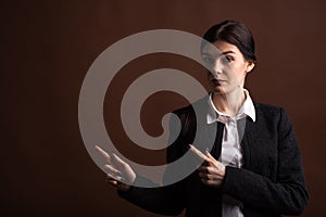 Portrait of serious brunette business woman pointing her finger to the side in studio on brown background with copyspace.