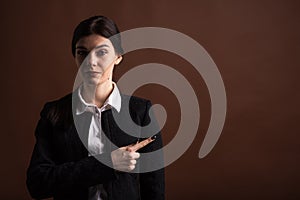 Portrait of serious brunette business woman pointing her finger to the side in studio on brown background with copyspace.